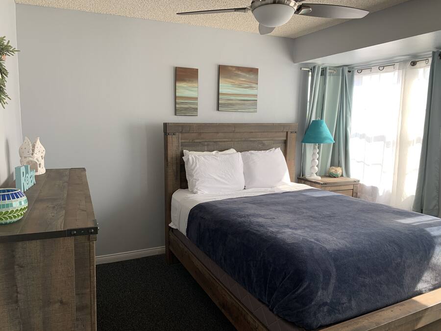 A bedroom with a wooden bed, a nightstand with a lamp, a desk with a decorative item, and two wall art pieces.