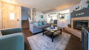 A living room with a sofa, coffee table, and fireplace. There is a staircase leading to another room. - Mandalay Shores Resort (Oxnard)