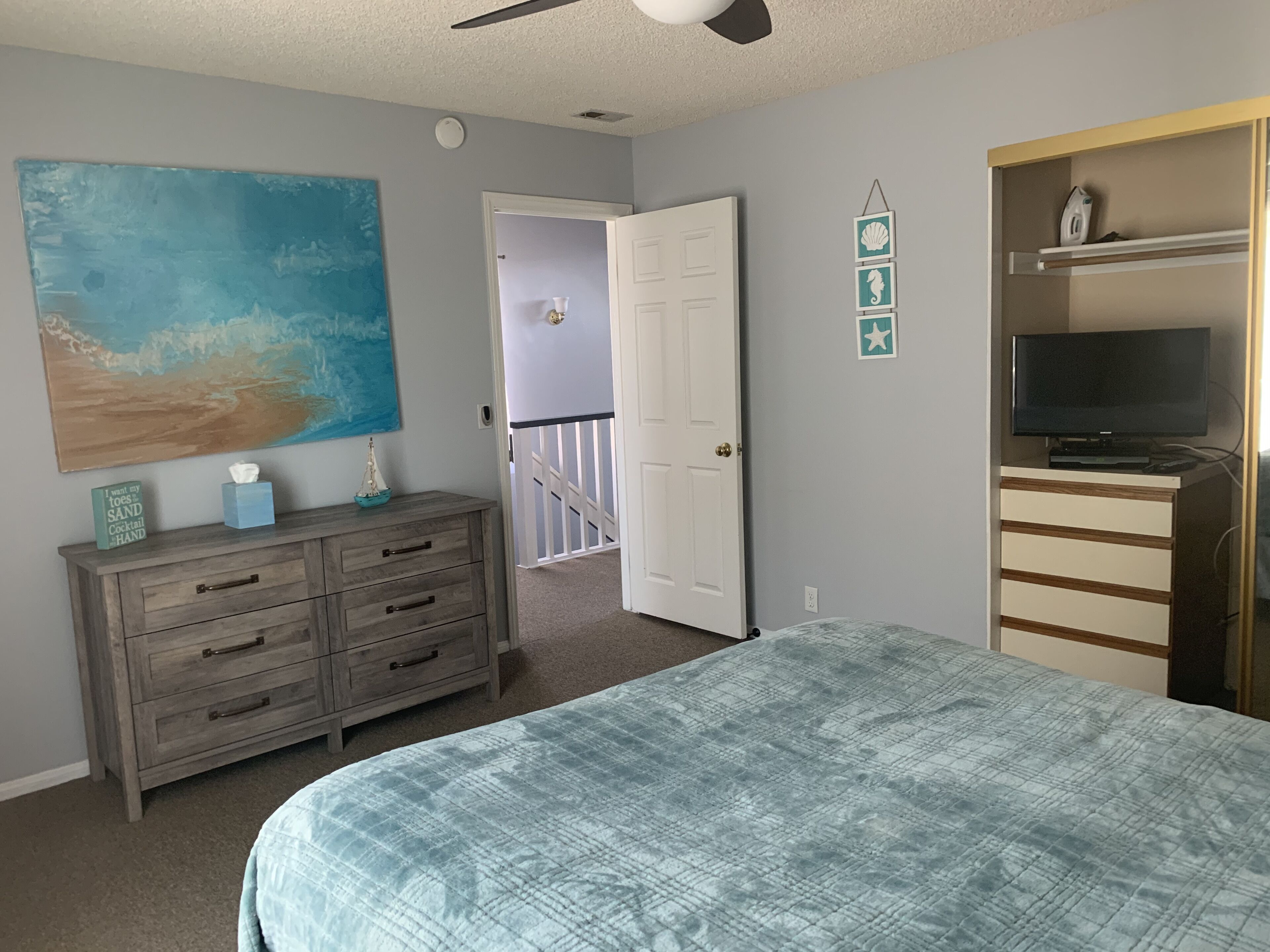 A bedroom with a bed, dresser, TV, and artwork.