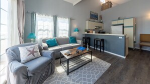 A modern living room with a sofa, a coffee table, and a kitchen area with a refrigerator and bar stools. - Mandalay Shores Resort (Oxnard)