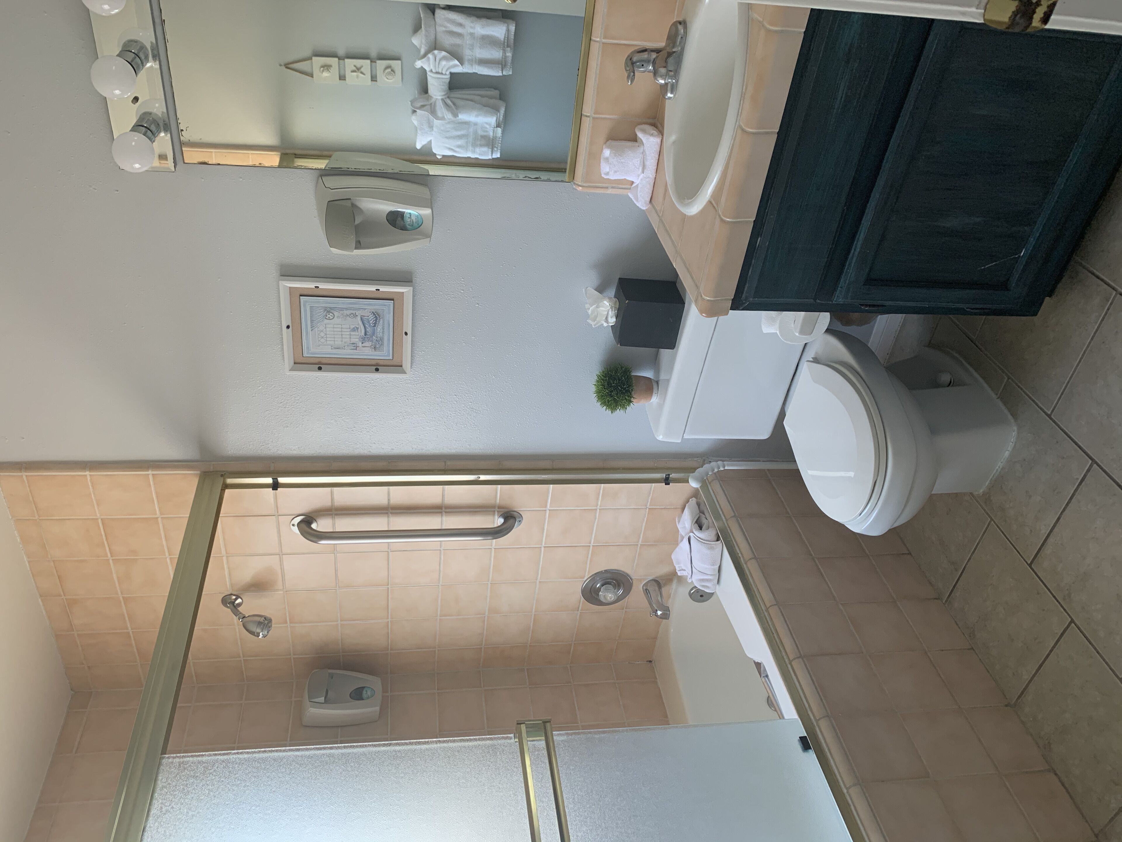 Een badkamer met toilet, wastafel, douche en een spiegel met verlichting.