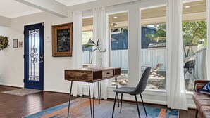 A living room with a wooden coffee table, a gray chair, a blue door, and a view of the backyard. - Designer’s home- Medical Center, Galleria, NRG. Lilly’s Maison 5 (Houston)