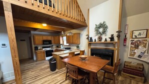 Una cocina amplia con pisos de madera, un comedor con mesa y sillas de madera, una zona de estar elevada y una chimenea.