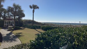 A gazebo with a tiled roof, surrounded by palm trees and a grassy area leading to a beach. - Updated Coastal Condo • Steps to Beach • Pool • King + Bunks • Ground Floor (Fort Walton Beach)