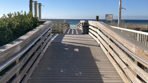 A wooden boardwalk leading to the ocean with railings and a trash can. - Updated Coastal Condo • Steps to Beach • Pool • King + Bunks • Ground Floor (Fort Walton Beach)