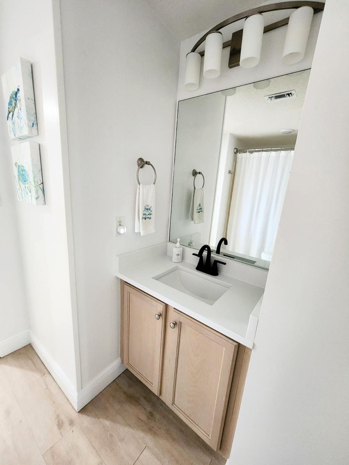 Een moderne badkamer met een witte wastafel, houten kastjes, een grote spiegel en een handdoekrek.