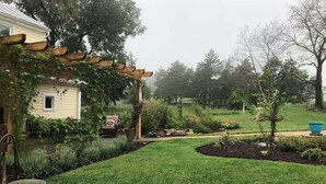 Um jardim bem cuidado com uma pérgola de madeira, um pequeno lago e diversas plantas e flores.