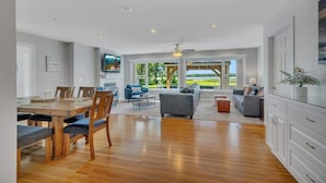 A spacious living area with a wooden dining table, comfortable seating, and a large window offering a view of the outdoors. - Lake Front Home with Pool and Stunning Views (Annandale)