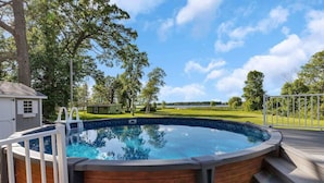 A hot tub with a wooden deck and a view of a grassy yard and trees. - Lake Front Home with Pool and Stunning Views (Annandale)