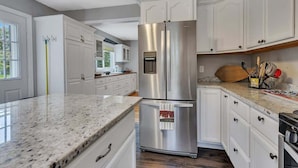 A modern kitchen with white cabinets, a stainless steel refrigerator, and a granite countertop. - Lake Front Home with Pool and Stunning Views (Annandale)