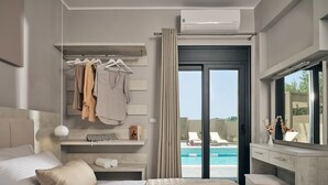 Una habitació d'hotel moderna amb llit, tocador amb mirall, prestatges penjants per a la roba i vista a una piscina.