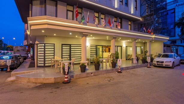 A hotel entrance with multiple flags, a covered outdoor seating area, and a parking lot. - Business Hotel Antalya (Antalya)