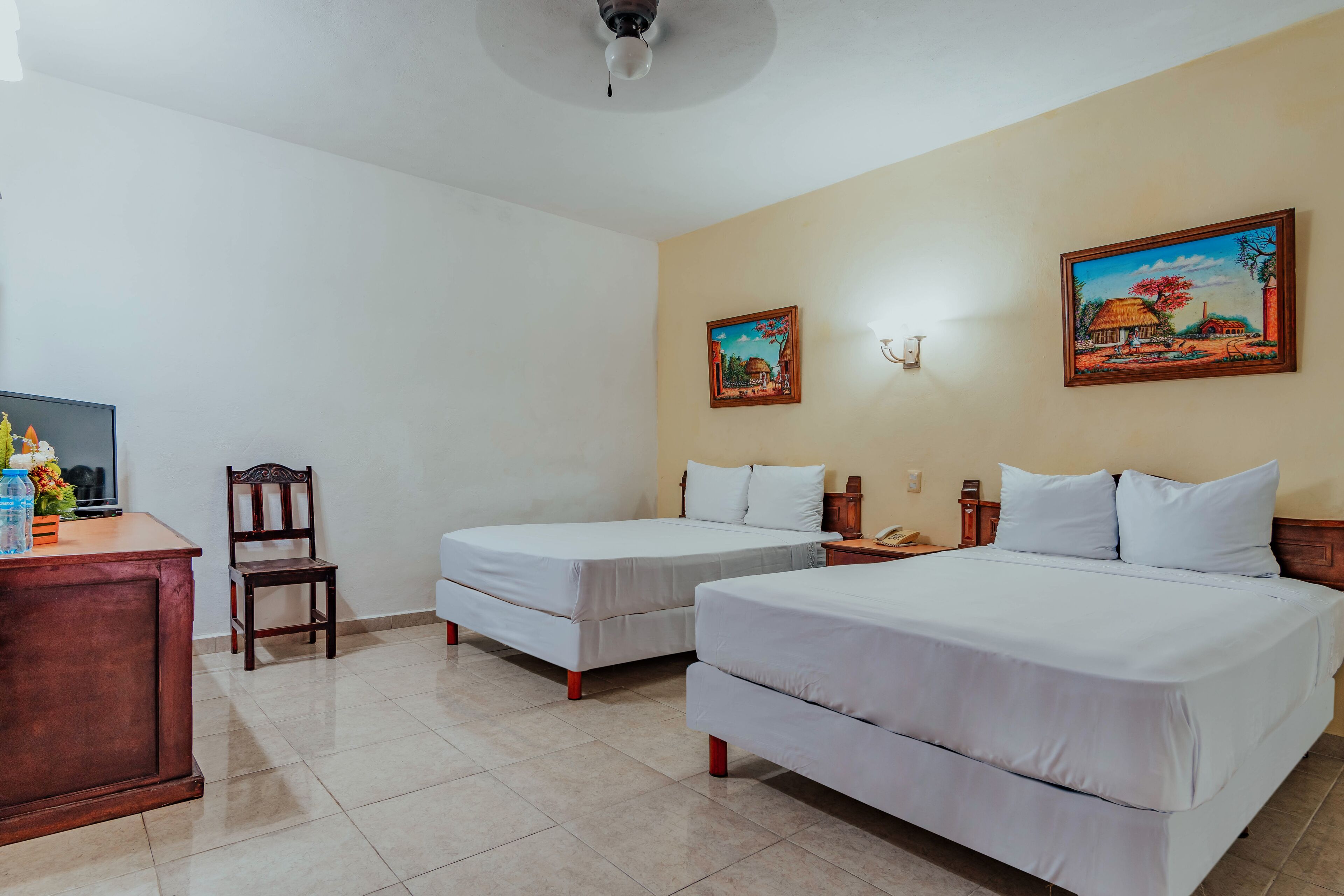 A hotel room with two single beds, a wooden desk, a chair, and a television.