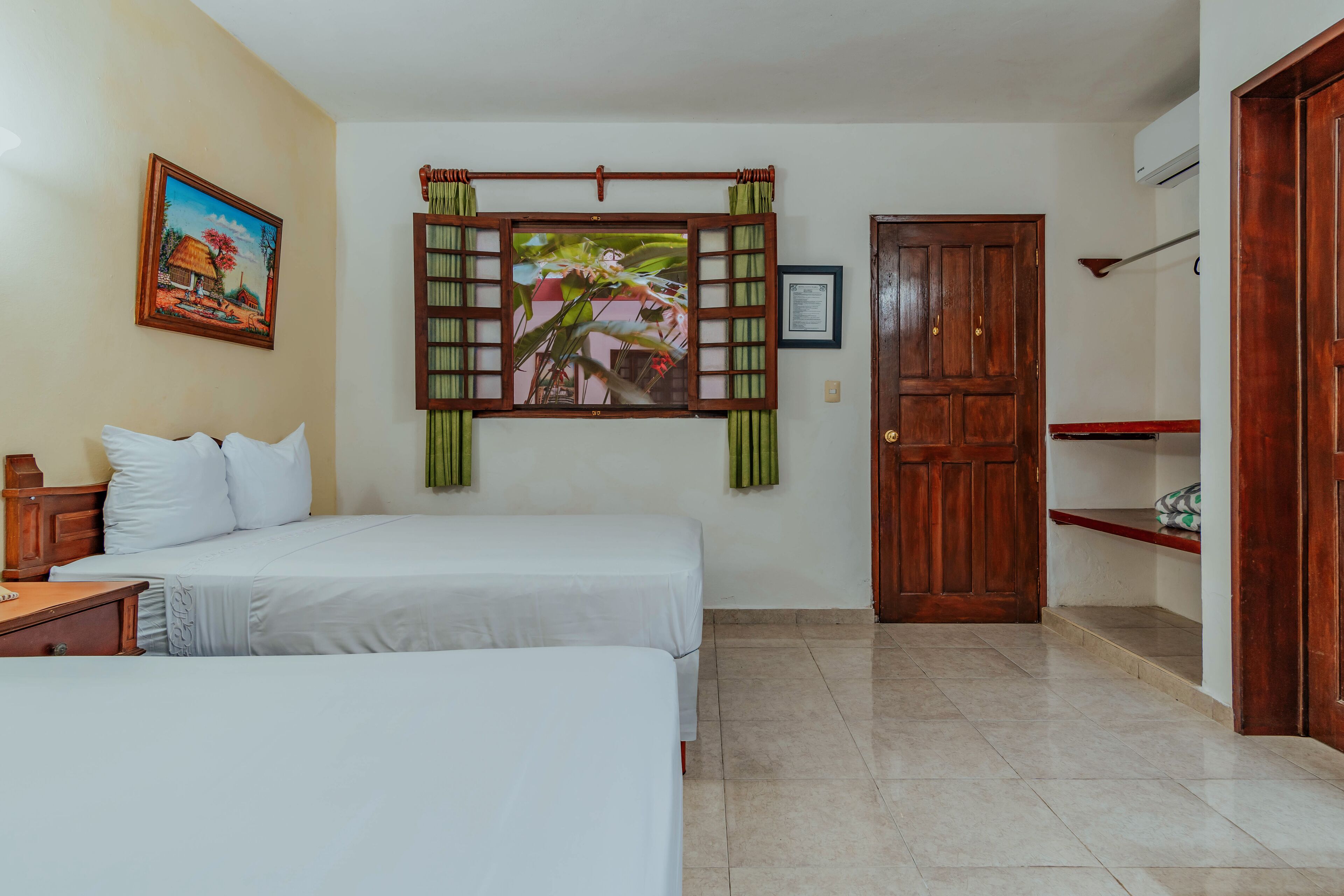 A hotel room with two beds, a painting, a wooden door, and a shelf.