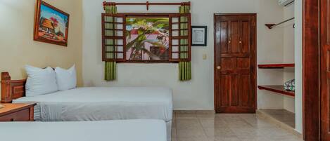 A hotel room with two beds, a painting, a wooden door, and a shelf.