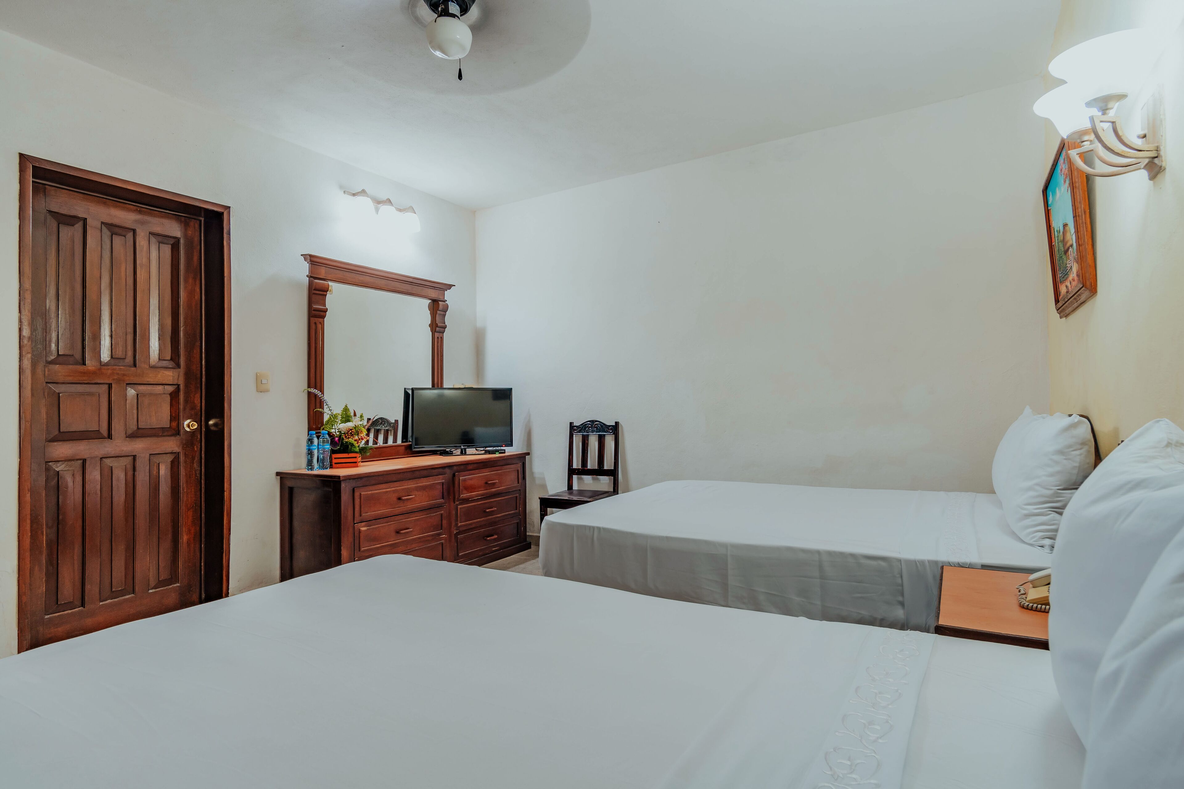 Une chambre d’hôtel avec deux lits, une commode en bois, un téléviseur et un ventilateur de plafond.