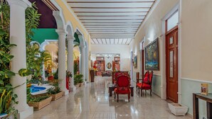 A spacious hallway with a tiled floor, a pool area on the left, and a seating area with red chairs on the right. - Hotel Santa María Mérida (Mérida)