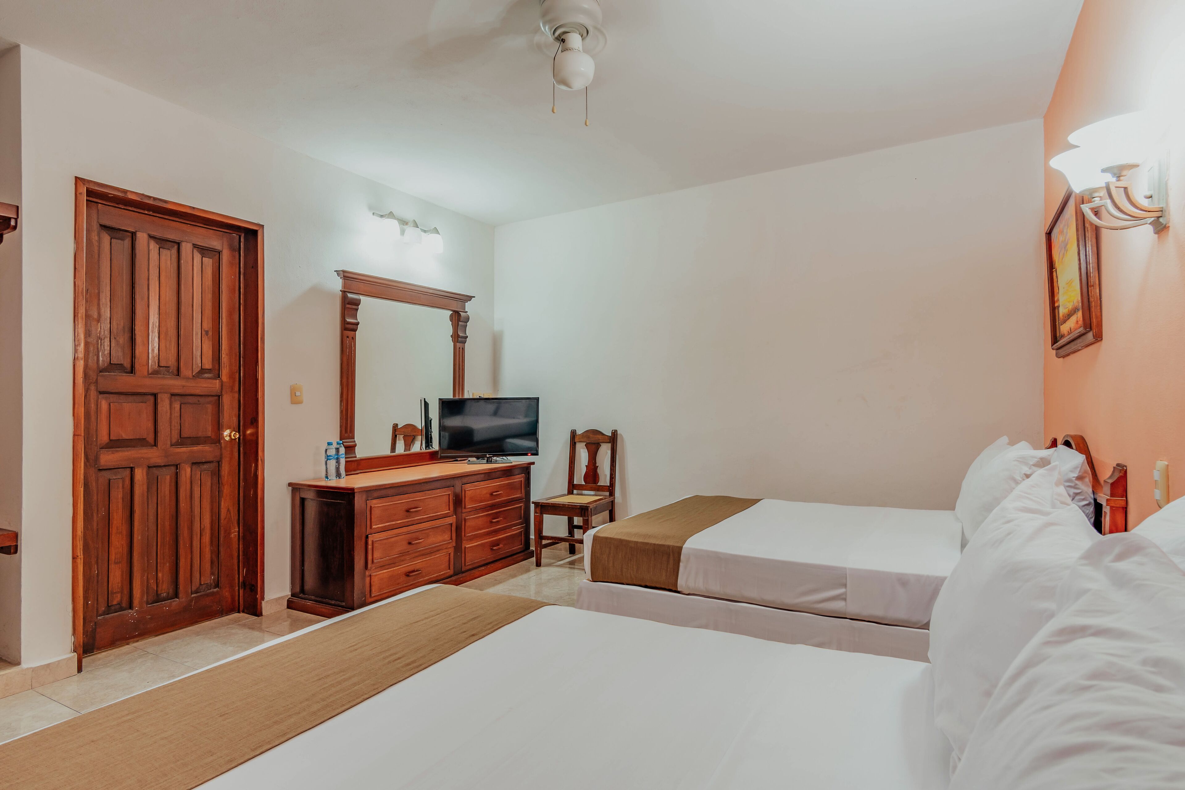 Habitación de hotel con dos camas, un aparador de madera, un televisor y un ventilador de techo.