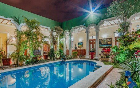 An indoor swimming pool with a tropical garden, a mural, and a sign indicating the pool's name.