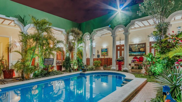 An indoor swimming pool with a tropical garden, a mural, and a sign indicating the pool's name. - Hotel Santa María Mérida (Mérida)