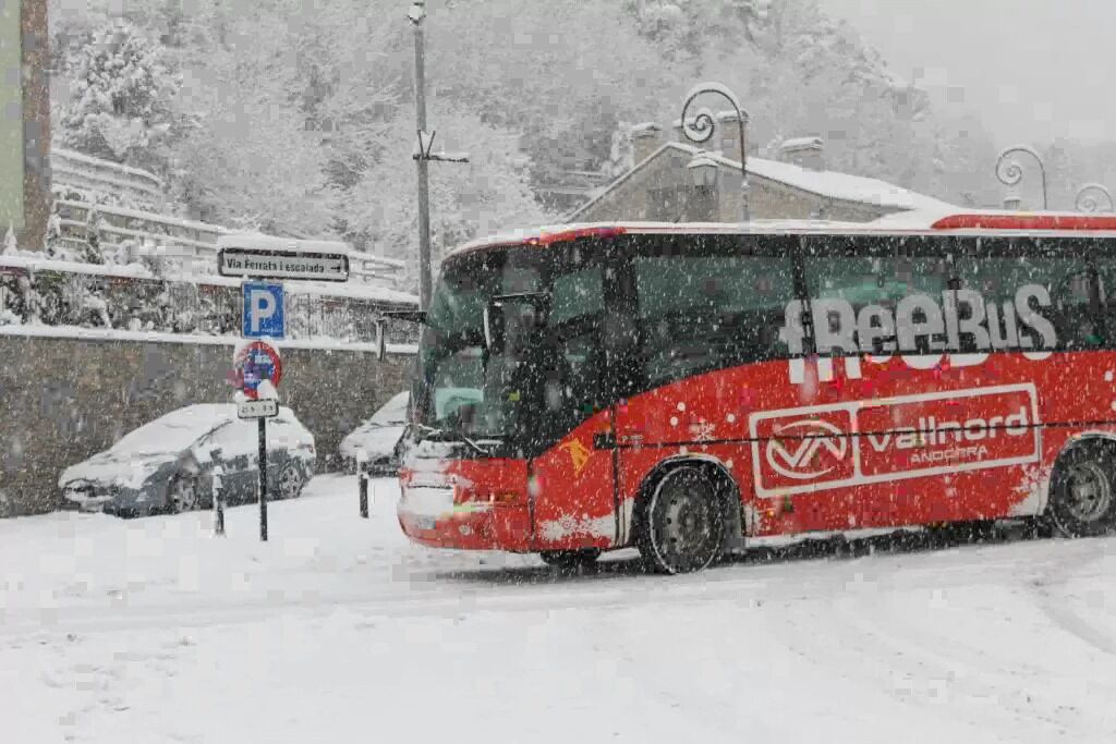 Un autobús rojo con los logotipos 'FreeBus' y 'Vallnord', estacionado en una carretera nevada.