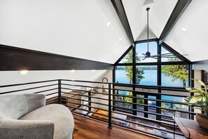 Un intérieur moderne donnant sur un lac, avec un canapé gris et un coin repas comprenant une table et des chaises.