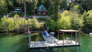 Une jetée dotée d ’un espace de repos abrité, d’un drapeau et d’une rampe d’accès pour bateaux, menant à une maison entourée d’arbres.