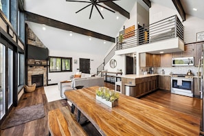 A spacious kitchen with a stone fireplace, wooden flooring, and a modern staircase.