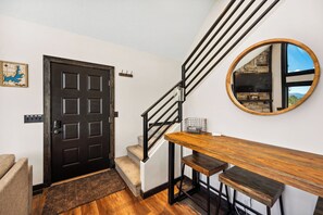 Un escalier avec une rampe noire, un banc en bois, un miroir rond et une porte décorée d’une carte.