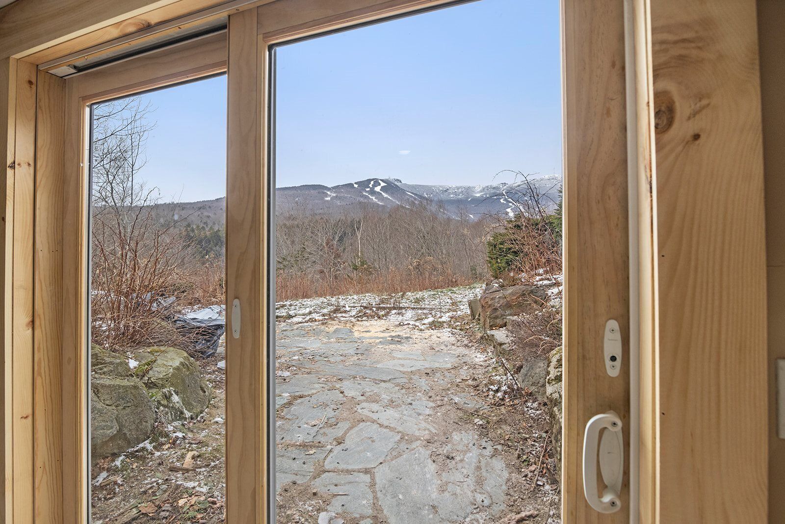 A wooden door with a view of a stone path leading to a mountainous landscape.