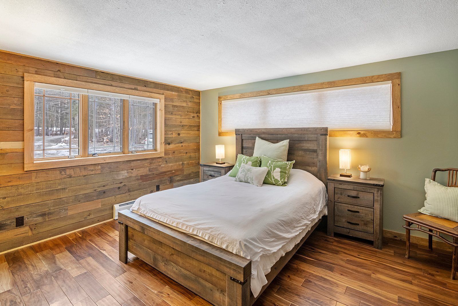 A bedroom with a wooden bed, two bedside tables, a nightstand, and a window with a view of trees.