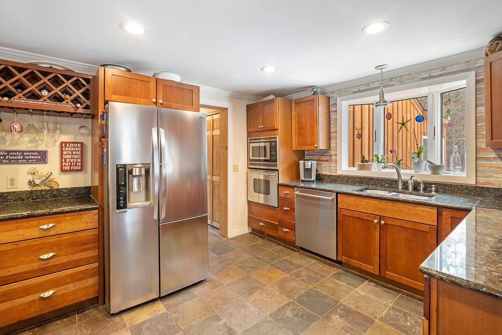 A modern kitchen with stainless steel appliances, wooden cabinets, and a stone tile floor.