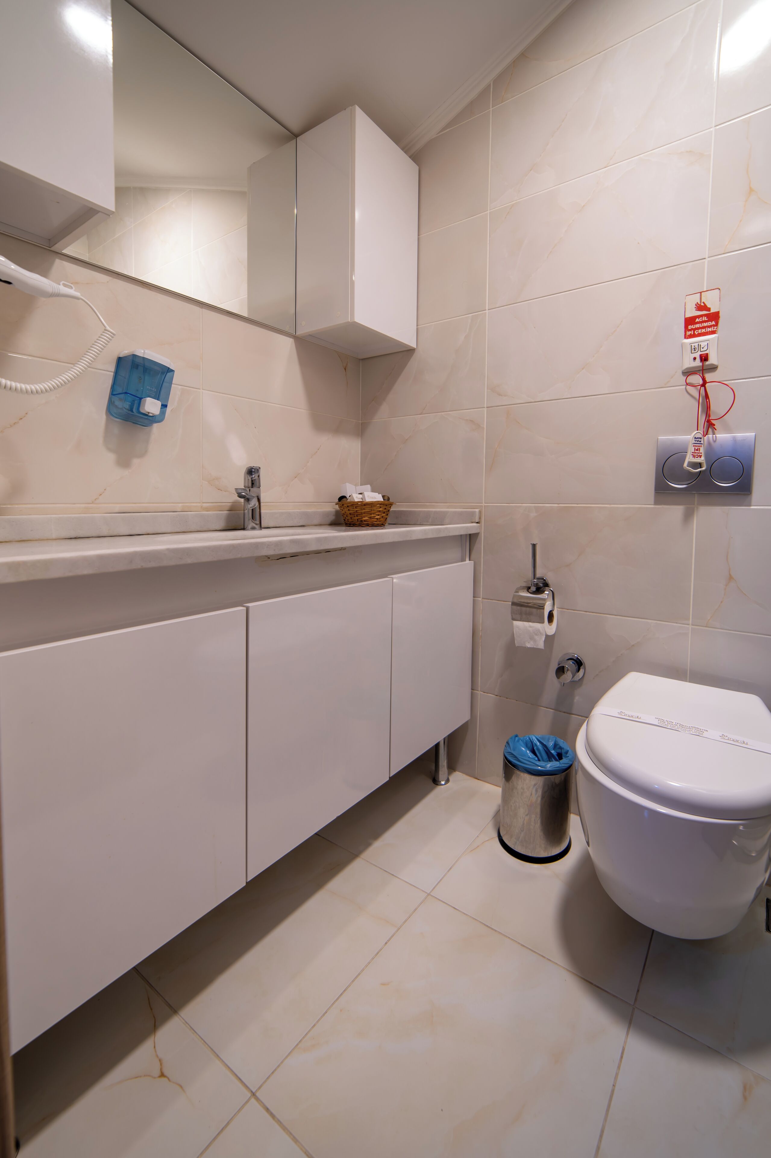 A bathroom with a white toilet, a sink with a mirror, and a trash bin.