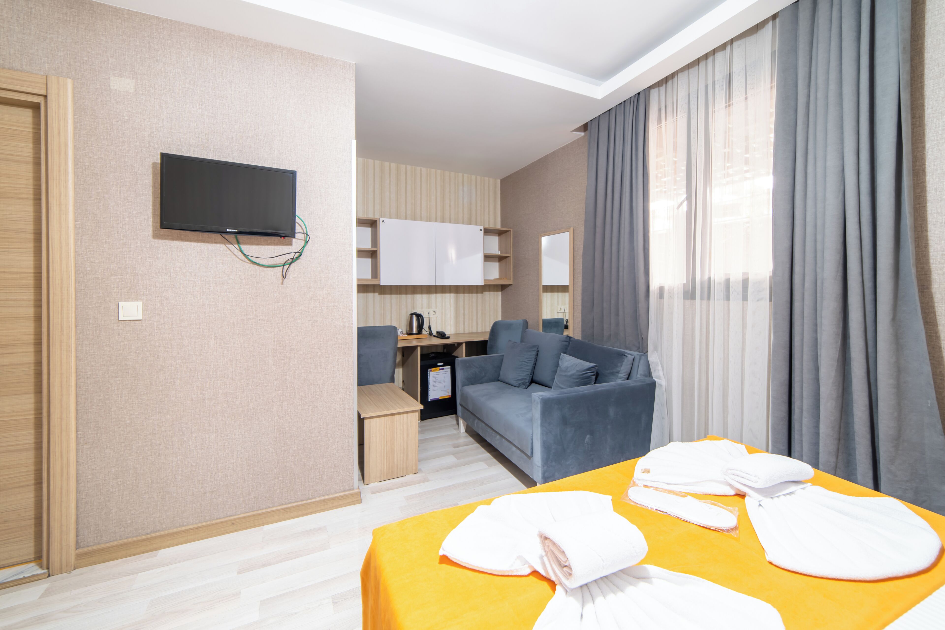 Habitació d'hotel amb llit, televisió penjada a la paret, escriptori amb cadira, sofà i finestra gran amb cortines.