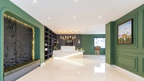 Un hall d’hôtel avec un sol en marbre, un comptoir d’accueil, une enseigne indiquant la réception, un mur au décor texturé et un tableau encadré accroché au mur.