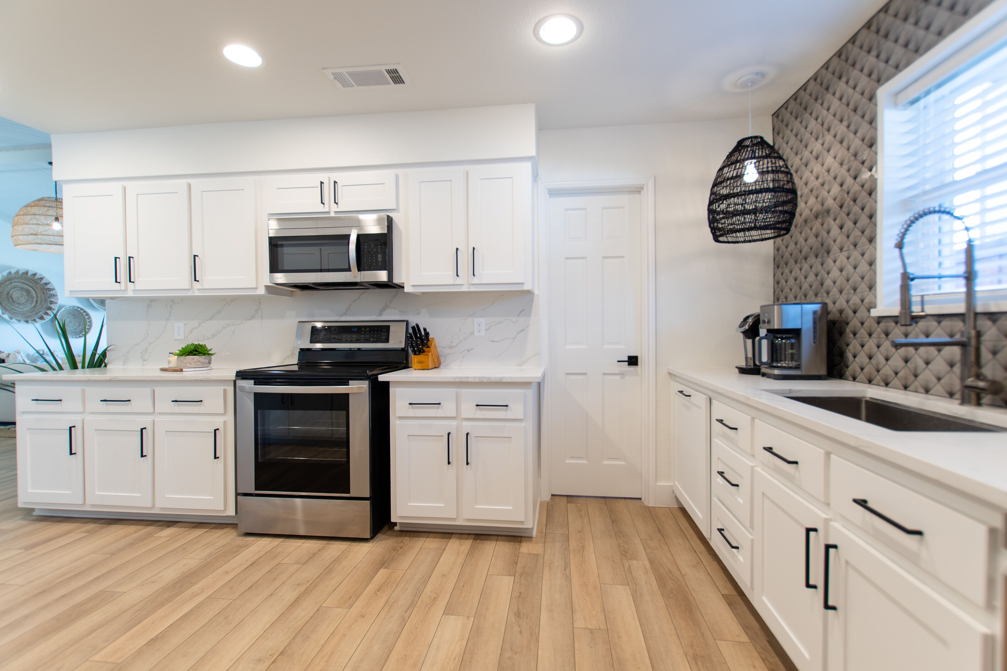 A modern kitchen with white cabinetry, stainless steel appliances, and a wooden floor.