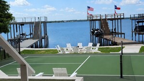 Een terras met zitplaatsen buiten, een tennisbaan en uitzicht op het water.