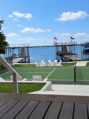 A deck with outdoor seating, a tennis court, and a view of the water.