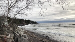 A rocky shoreline with a wooden staircase leading to a building, surrounded by trees and the ocean. - Superior Reflections  Cabin #2 on Lake Superior (Schroeder)