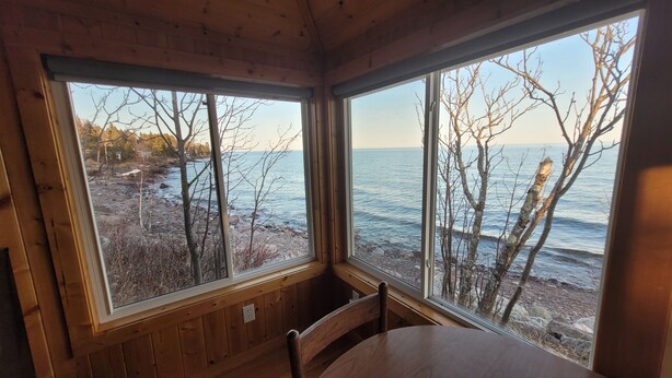 A cabin with two large windows overlooking a rocky shoreline and a body of water. - Superior Reflections  Cabin #2 on Lake Superior (Schroeder)