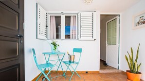 Ein kleiner Raum mit Tisch und Stühlen, einer Topfpflanze und einem Fenster mit Vorhängen.