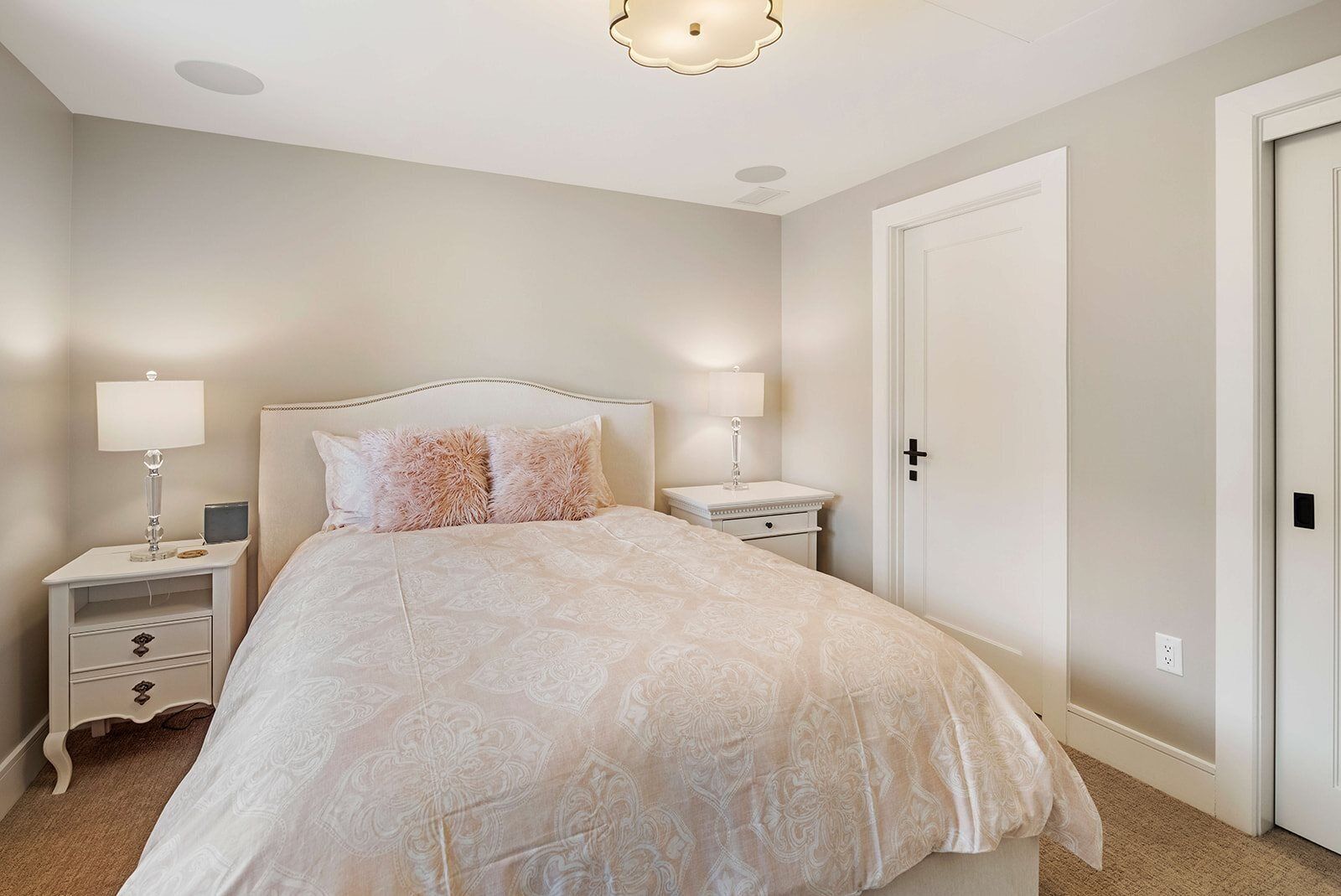 A bedroom with a bed, two bedside tables, a nightstand, a door, and a ceiling light fixture.