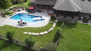 A two-story house with a backyard featuring a swimming pool, patio furniture, and a stone border.