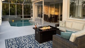 Un área de piscina con un patio con paredes de vidrio, una chimenea y mobiliario exterior.