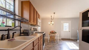 Una cocina con armarios de madera, un lavamanos, una estufa y una mesa de comedor con sillas.
