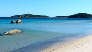 A beach with clear water, a sandy shore, and distant hills.