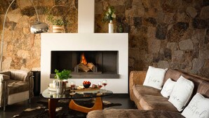 A cozy living room with a stone wall, a fireplace, a leather sofa, and a glass coffee table with snacks and drinks.
