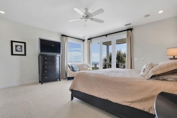 A bedroom with a bed, a ceiling fan, a TV, a dresser, and a view of the outdoors.