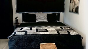 Un dormitorio con una cama grande, cabecera negra, colcha acolchada y un taburete de madera.