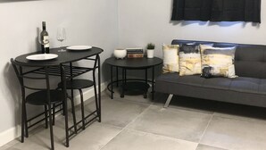 Un espacio habitable pequeño con una mesa de comedor, sillas, un sofá, un televisor montado en la pared y una ventana con cortinas.